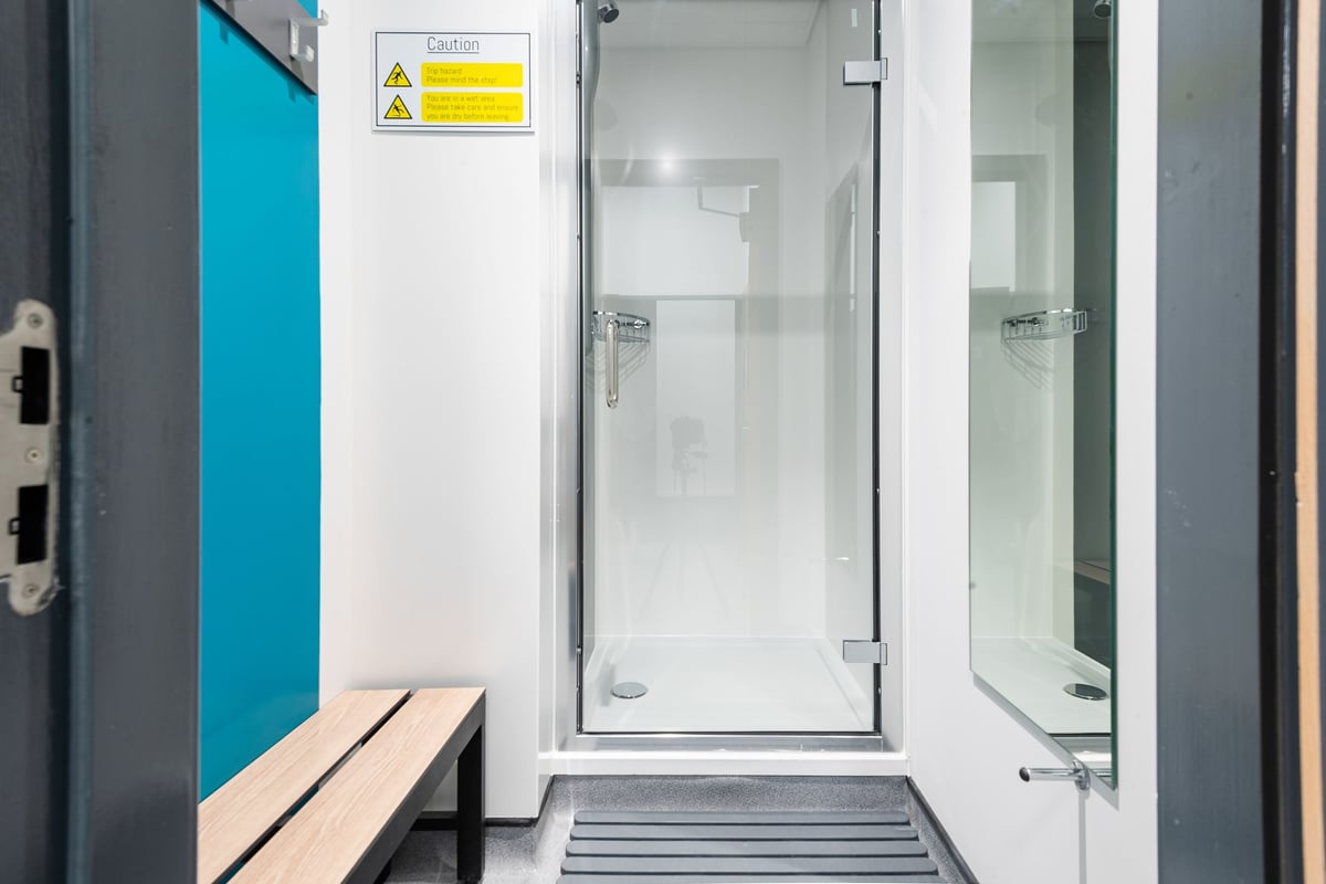PureGym Elgin: Shower cubicles, benches, hazard signage - appears to be changing room facilities.