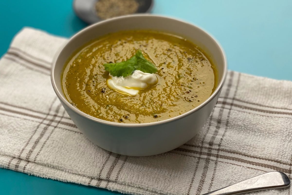 Bowl of squash and carrot soup topped with cream and herb leaf on striped cloth