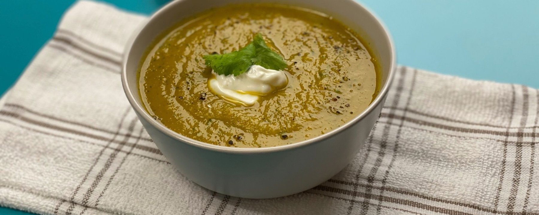 Bowl of squash and carrot soup topped with cream and herb leaf on striped cloth