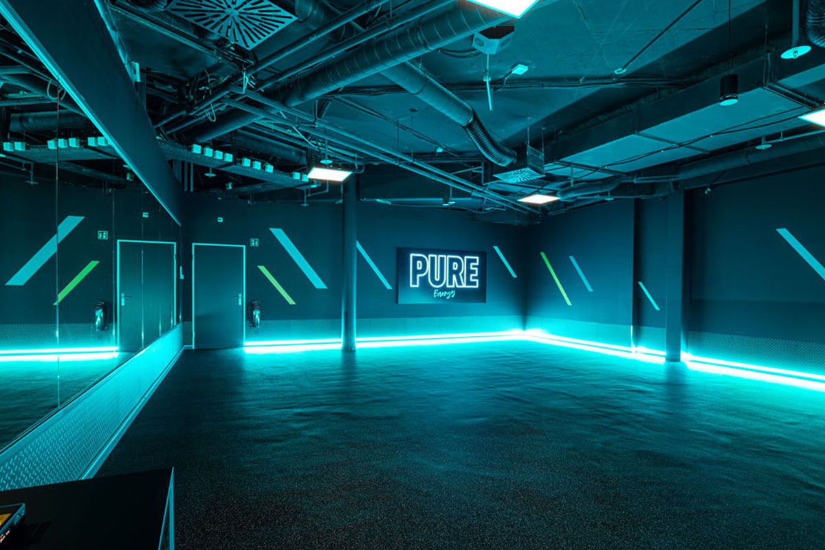 PureGym Lausanne Prilly: Gym studio with neon blue lighting and rubberized flooring.