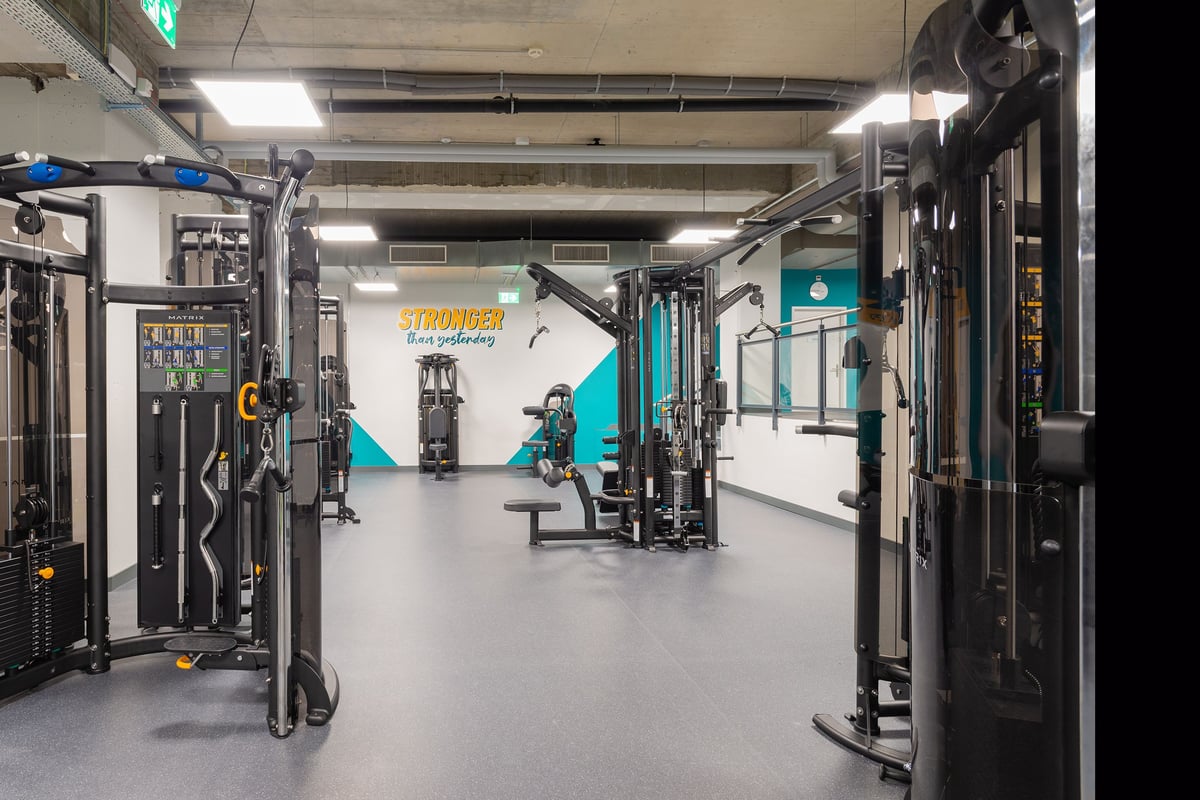 PureGym La Chaux-de-fonds: Strength training area with cable machines, weight racks, benches, and rubberized flooring.