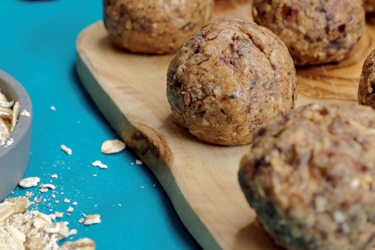 Energy balls on a wooden board with oats and dates on a blue surface nearby
