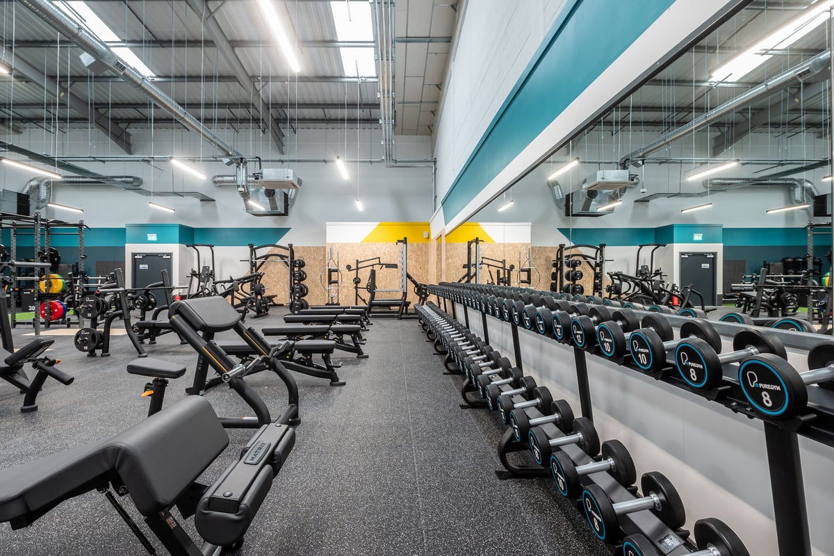 PureGym Thamesmead: Rows of weight benches, resistance machines, free weights, and flooring in a brightly lit gym.