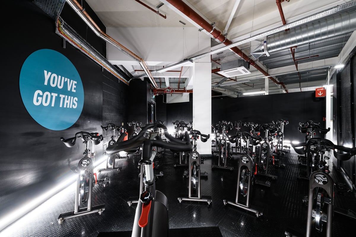 PureGym Cambridge Grafton Centre: Rows of stationary bikes, dimly lit space with motivational signage on the wall.