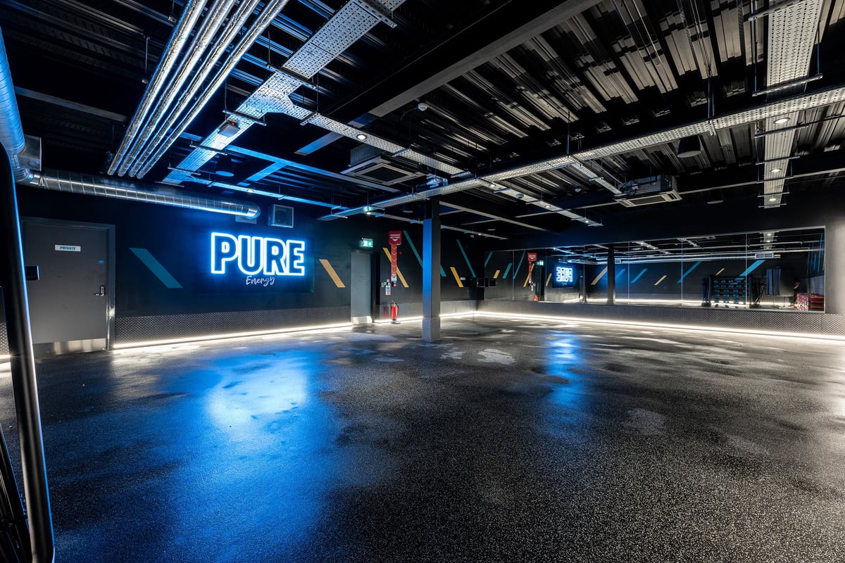 PureGym Coleraine: Blue-lit studio with mirrored wall and PURE Energy wall art.