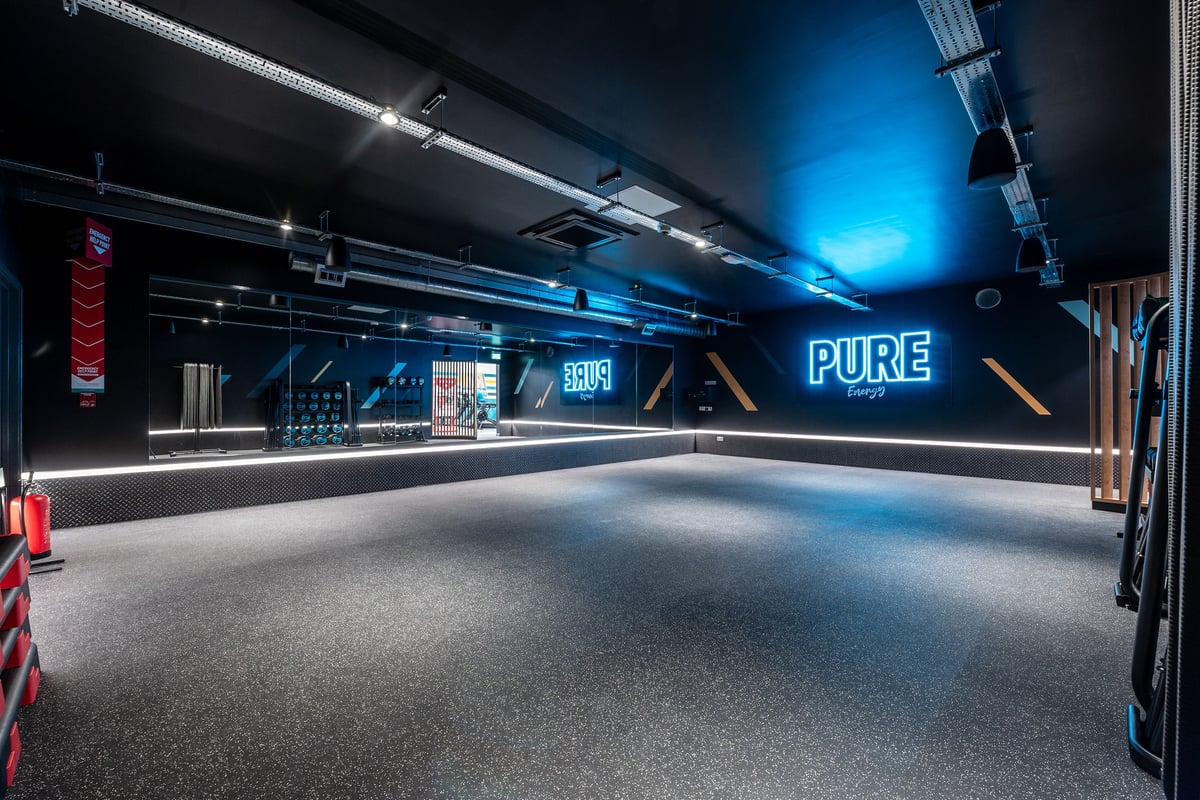 PureGym Thamesmead: Blue-lit studio space with rubberised flooring and PURE branding signage.