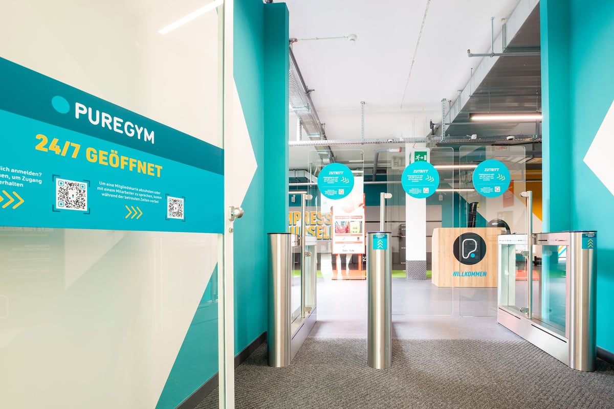 PureGym Wil: Zone d'entrée avec signalisation, accents turquoises et portes d'entrée menant aux espaces de remise en forme.