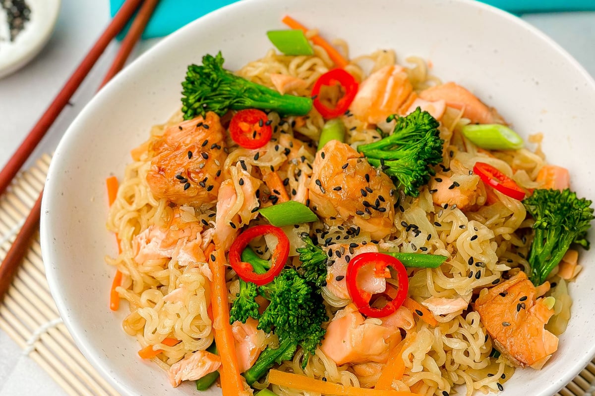 Bowl of noodles with salmon, broccoli, red chilli and black sesame seeds