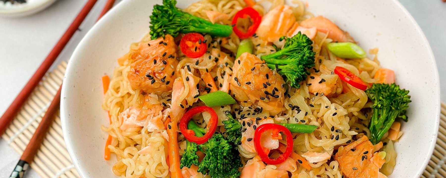 Bowl of noodles with salmon, broccoli, red chilli and black sesame seeds