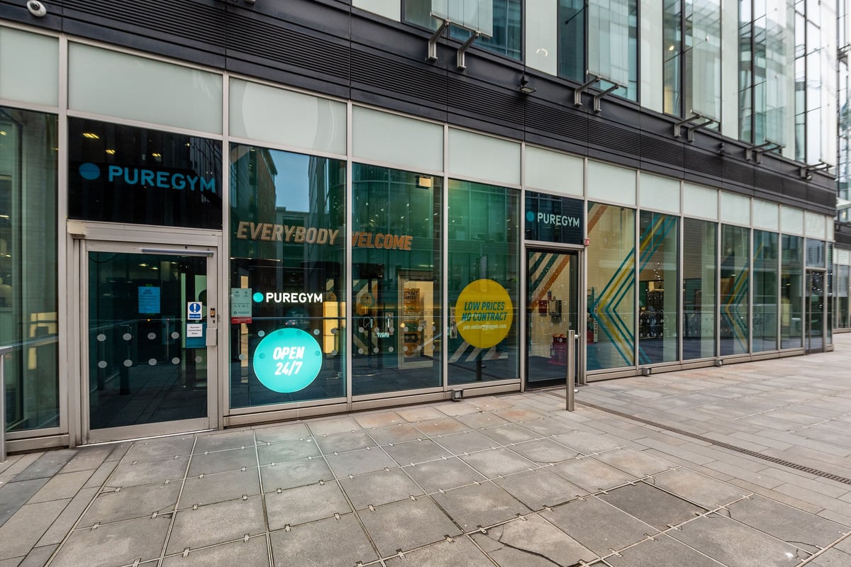 PureGym Manchester Spinningfields: Gym exterior with large glass windows showcasing exercise equipment and interior space.