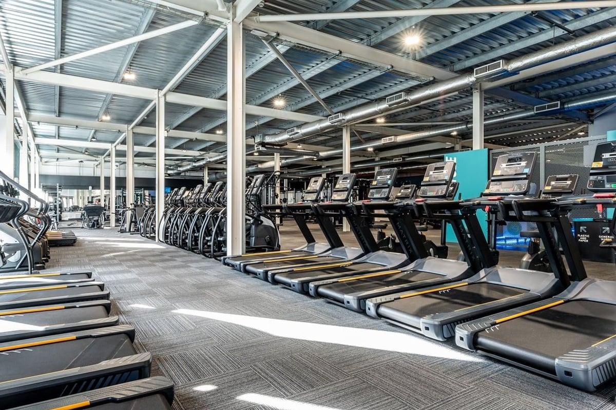 PureGym Bristol Union Gate: Rows of treadmills in a well-lit gymnasium with open ceiling structure and supporting pillars.