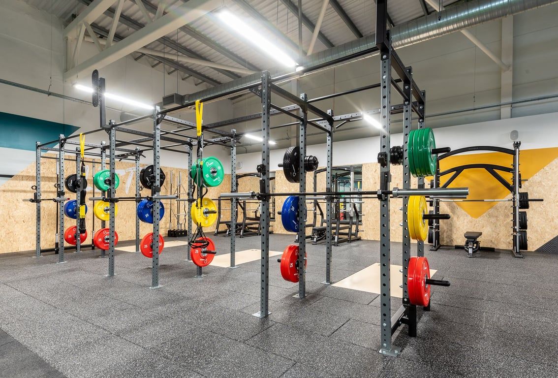 PureGym Barnsley: Rig with weight plates in varied colours, bars, squat racks, and rubber flooring.