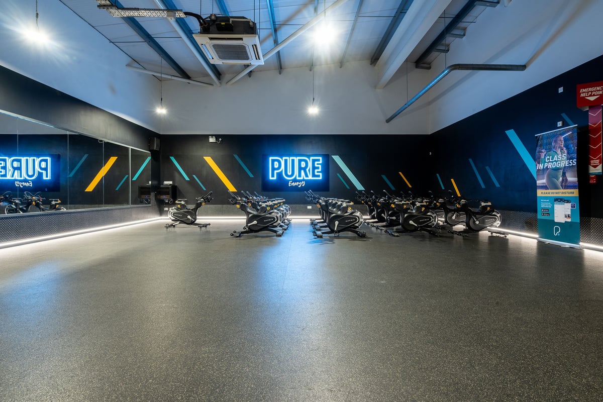 PureGym Aberdeen Kittybrewster: Rows of stationary bikes on rubberized flooring in a dimly lit studio.
