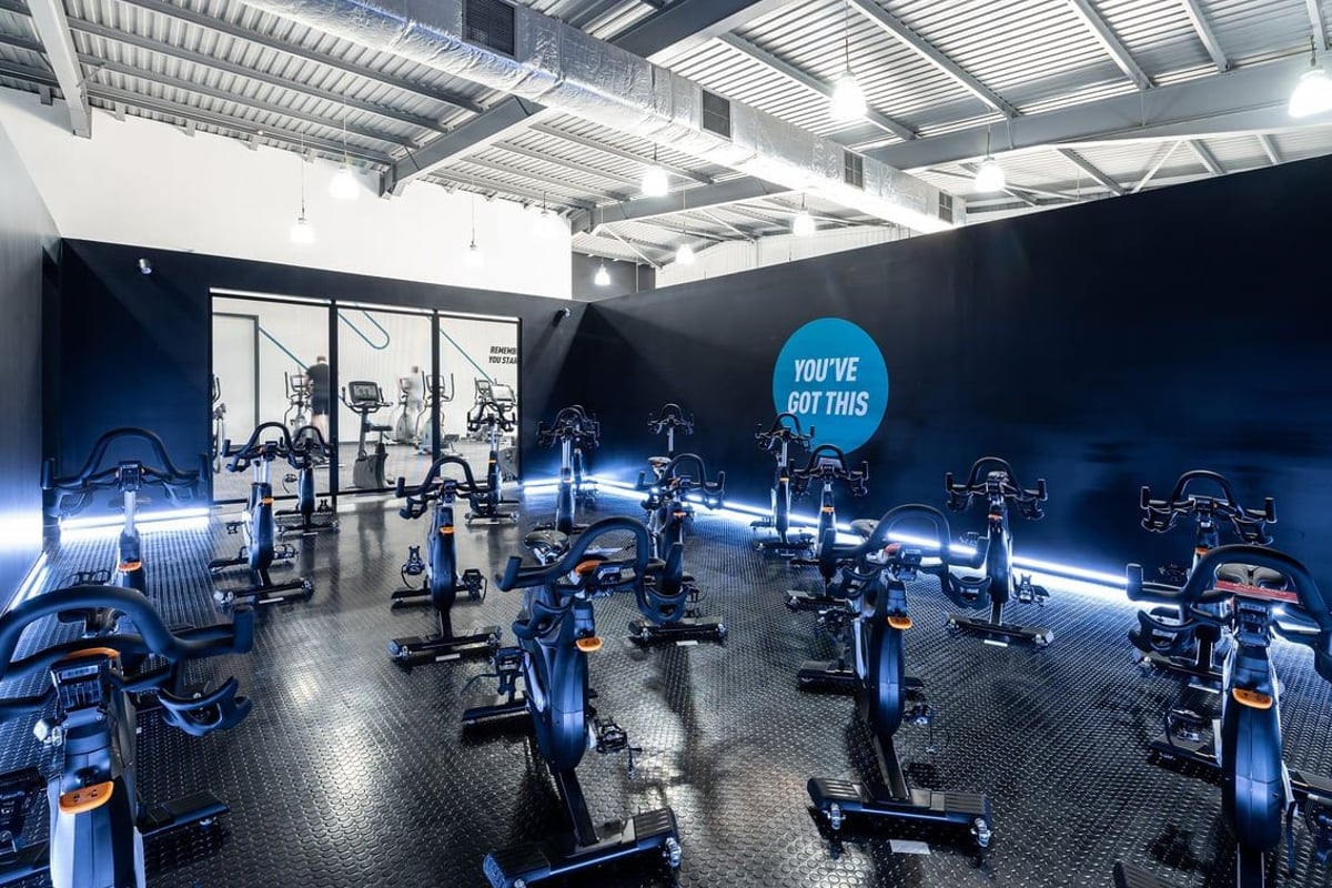 PureGym Warrington Central: Rows of stationary bikes, neon blue lighting, and motivational signage in a darkened gym studio.