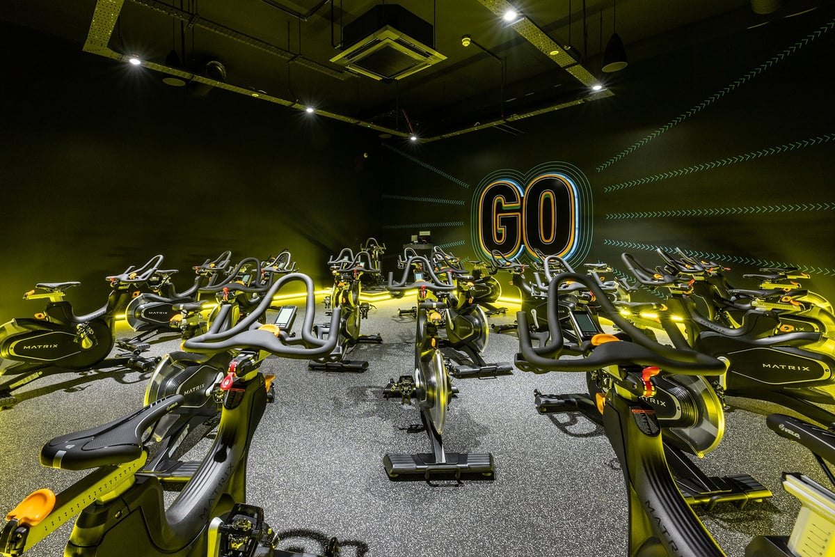 PureGym London Feltham: Rows of stationary cycles, neon signage "GO", and dimly lit studio space.