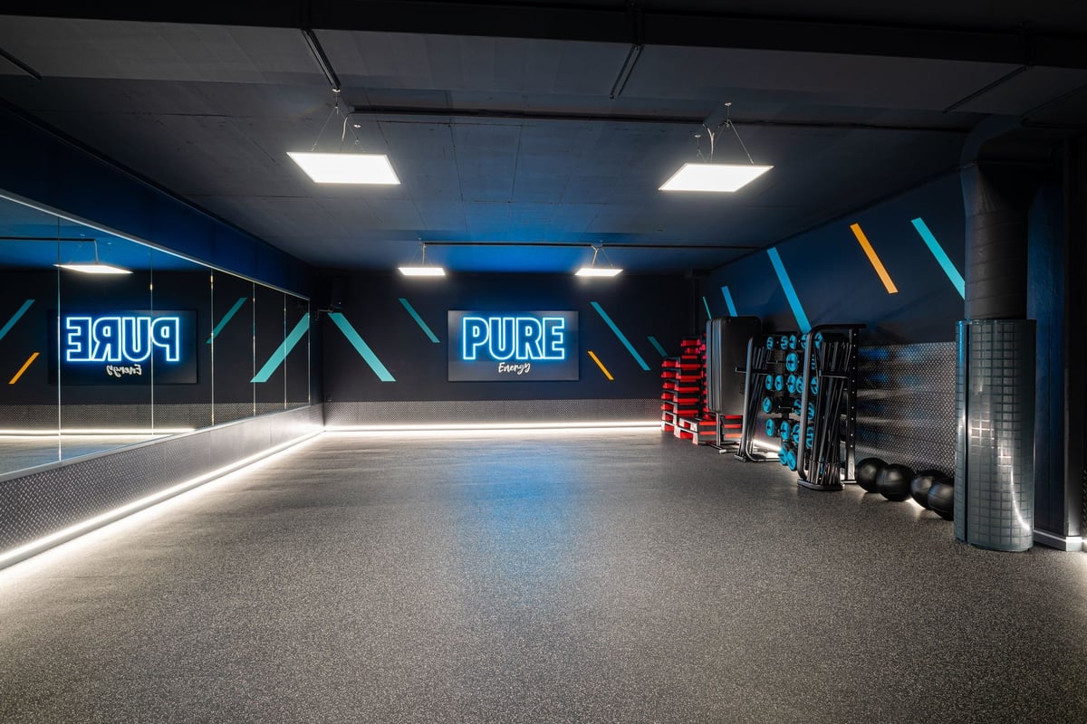 PureGym Altstetten: Ein schwach beleuchtetes Pure Gym-Studio mit Neonbeschilderung, Hantelständern und
