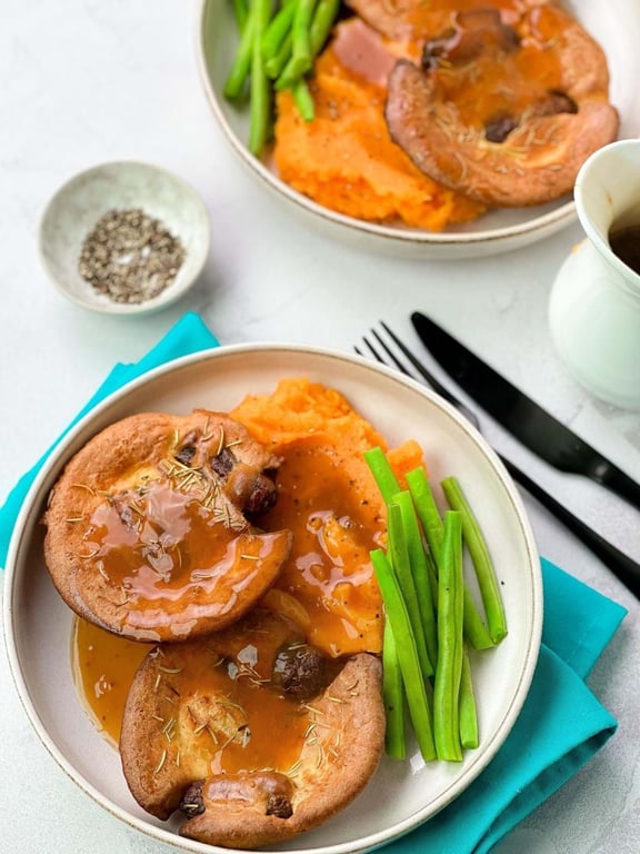 Yorkshire puddings with gravy, mashed sweet potatoes, and green beans on plates