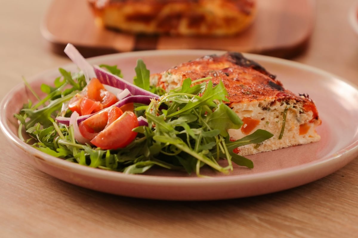Slice of frittata with rocket salad, tomato and red onion on pink plate