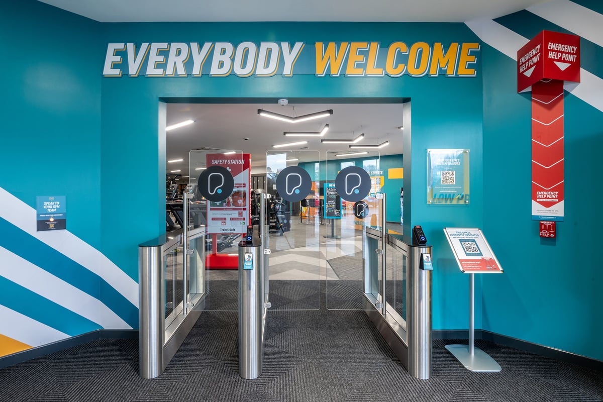 PureGym Airdrie: Entrance area with turnstiles, teal walls proclaiming "Everybody Welcome" sign.
