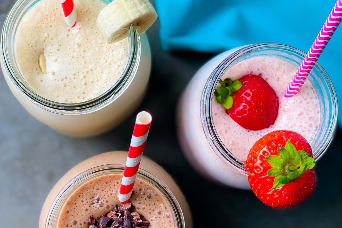 Three smoothies in jars with striped straws, topped with banana slice, strawberries