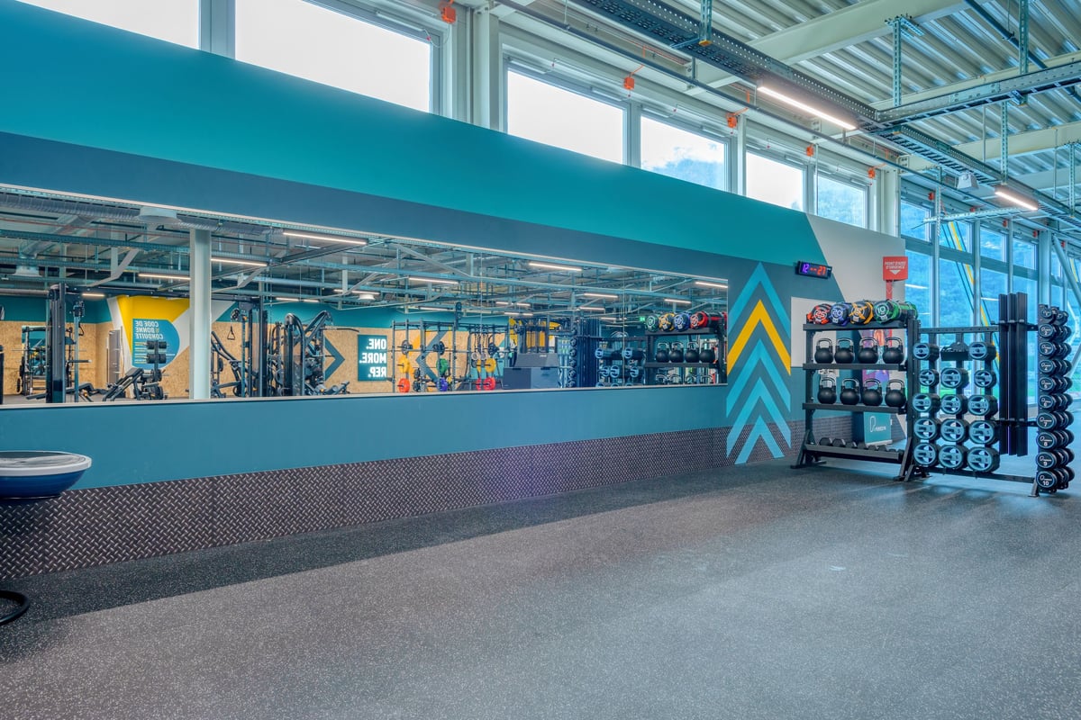 PureGym Martigny: Fitnessstudio mit Plattformen für Gewichtheber, Hockstützen, Hantelbäumen und gummiertem Boden.
