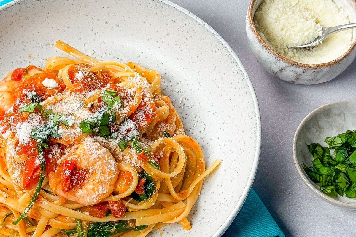 Linguine with prawns and tomato sauce topped with grated cheese and fresh basil