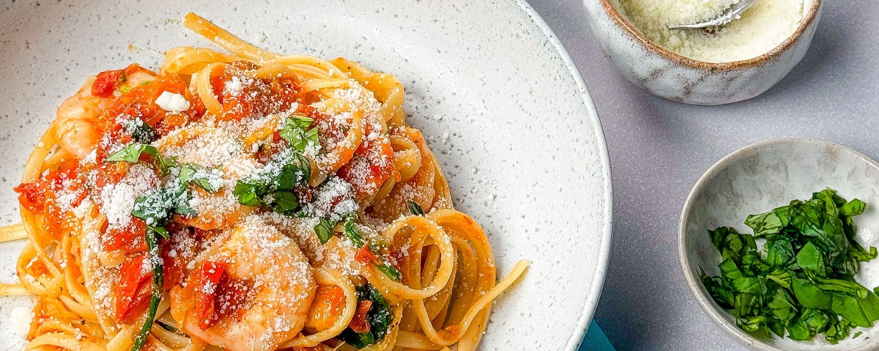 Linguine with prawns and tomato sauce topped with grated cheese and fresh basil