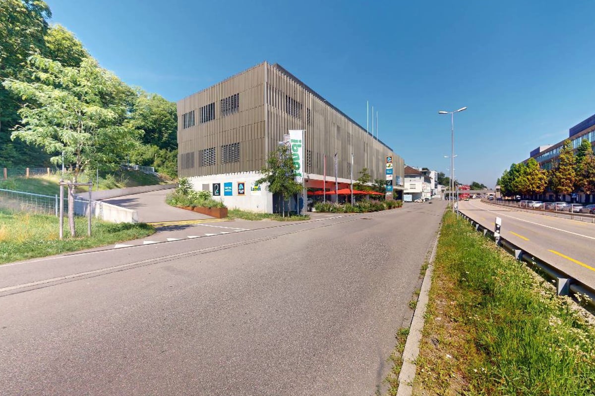 PureGym Adliswil: Vue extérieure sur la rue, bâtiment avec vitrines, route avec véhicules et lampadaires.
