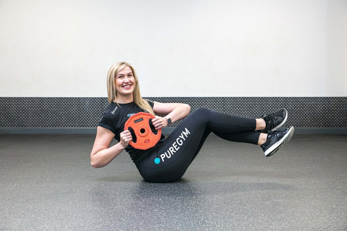 Woman in gym clothes holding a weight plate while balancing on her back with legs raised