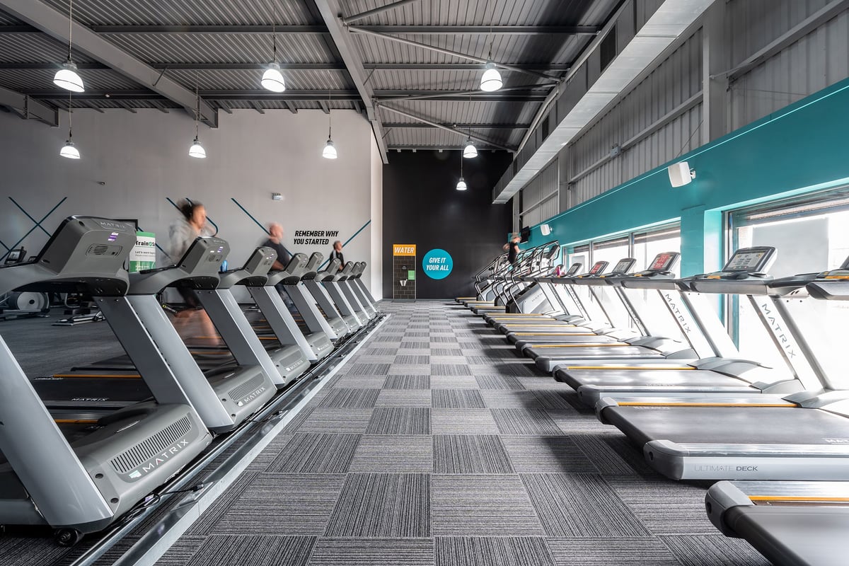 PureGym Warrington Central: Rows of treadmills in a dimly lit gym interior with pendant lighting.