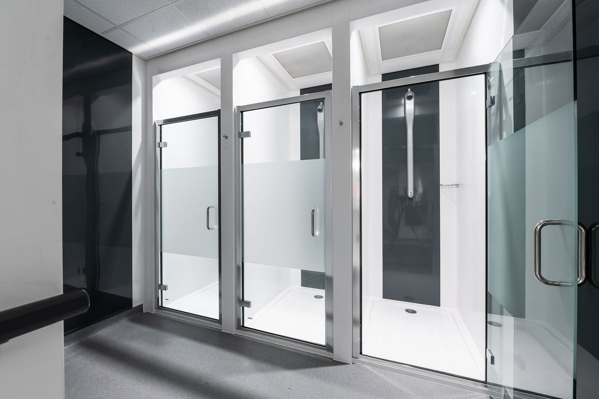 PureGym Puregym Crayford: Shower stalls with glass doors, tiled floors, and bright fluorescent lighting.