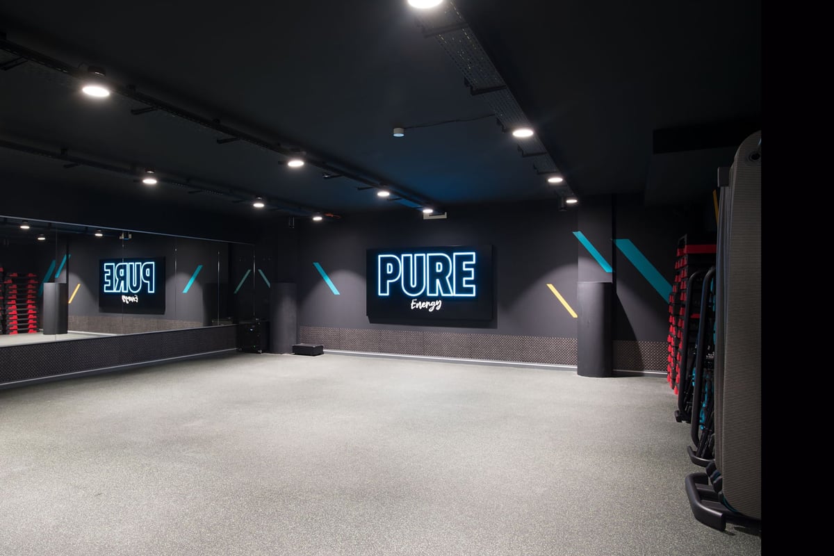 PureGym Lyss: Un studio de fitness pur avec des murs noirs, des miroirs de sol, des supports d'équipement et des accents de marque bleus et rouges.