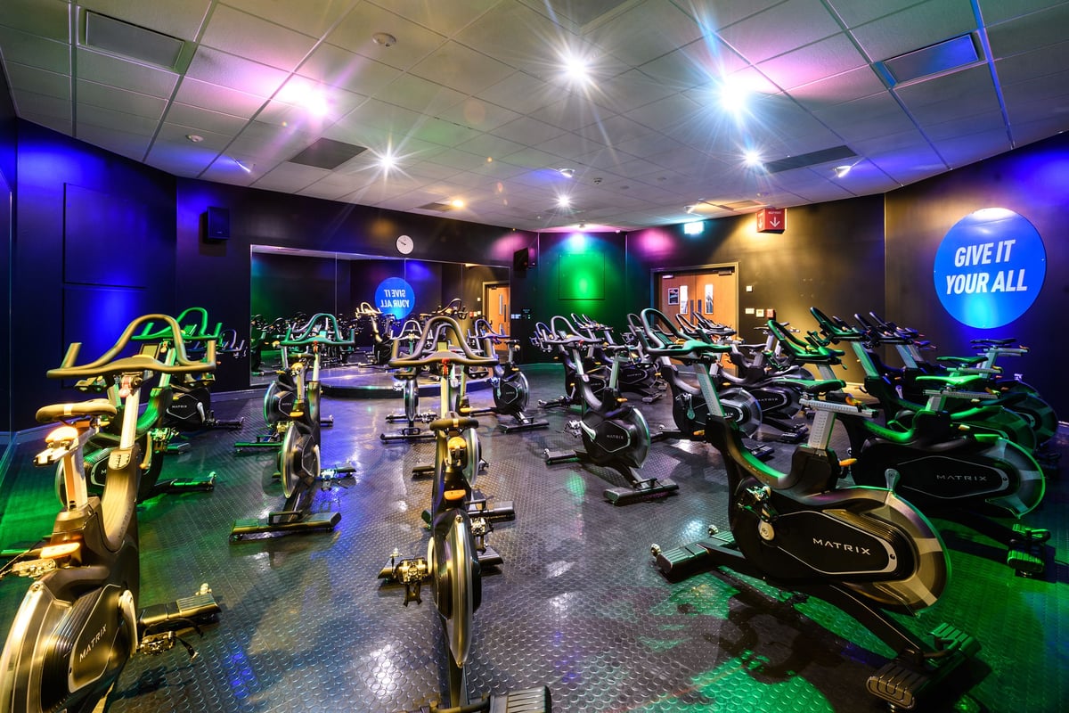 PureGym Aylesbury: Rows of stationary bikes, treadmills, ellipticals under neon lighting in a modern fitness studio.