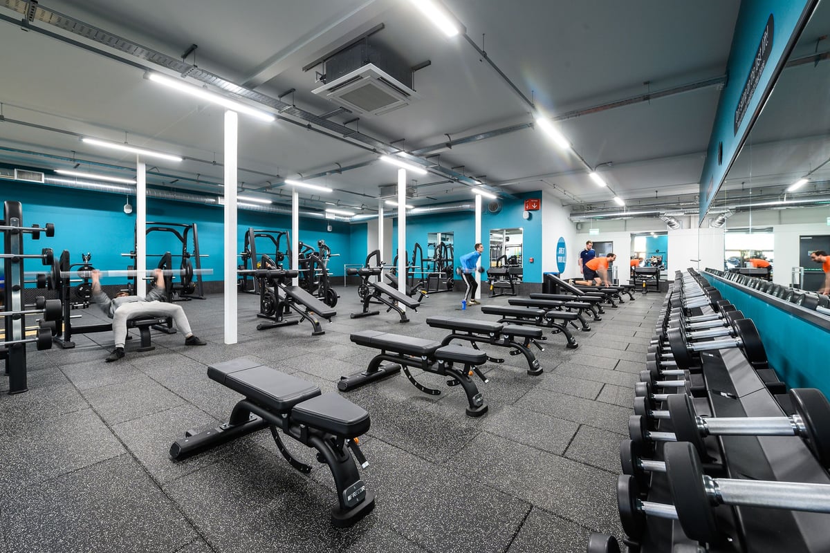 PureGym Exeter Bishops Court: Weight racks, benches, dumbbells, and exercise machines in a teal-colored gym interior.