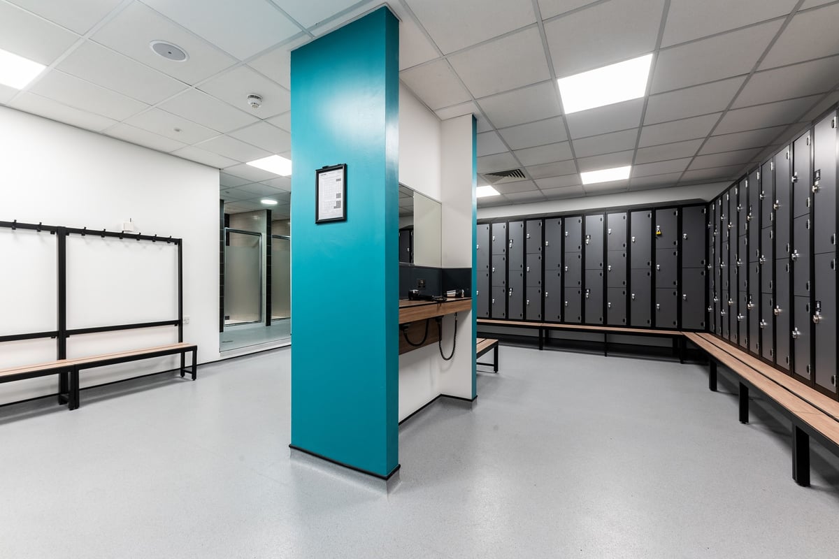 PureGym Nottingham Beeston: Locker room with benches, metal lockers, and changing area cubicles.