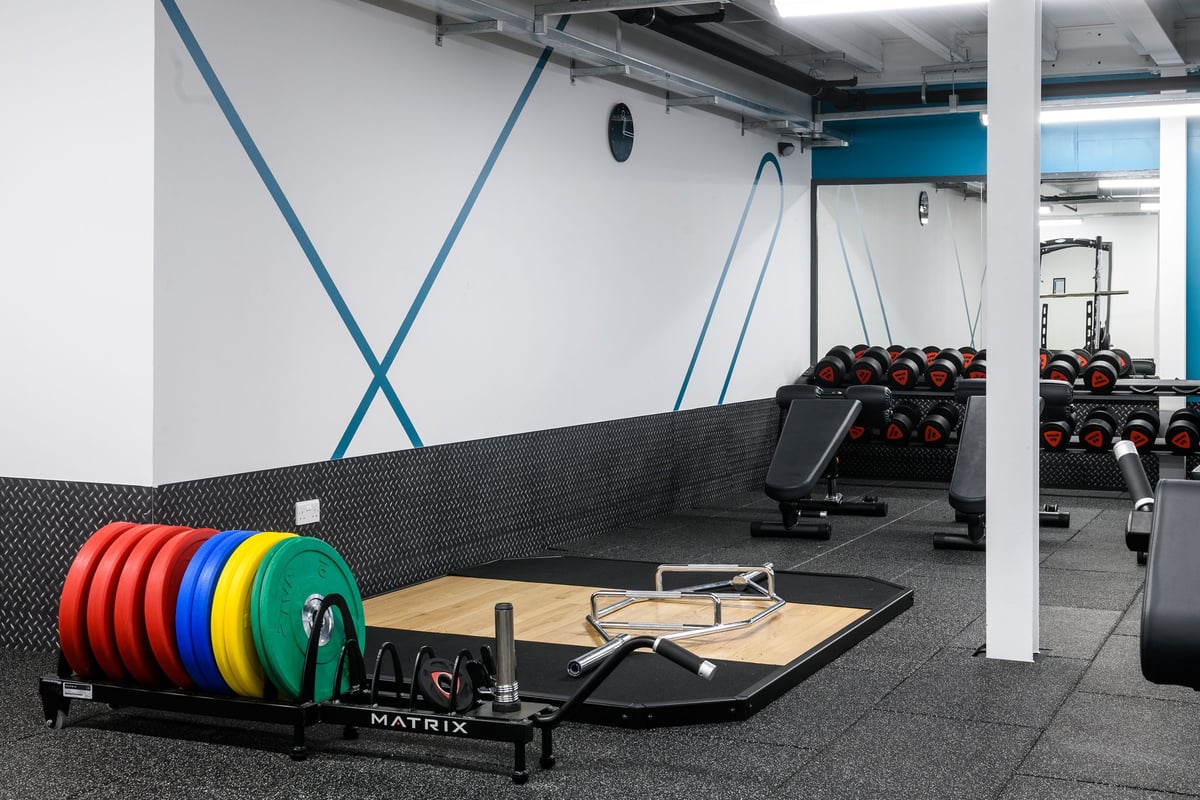 PureGym Glasgow Silverburn: Weightlifting platform, coloured bumper plates, dumbbell racks, and resistance machines in a gym.