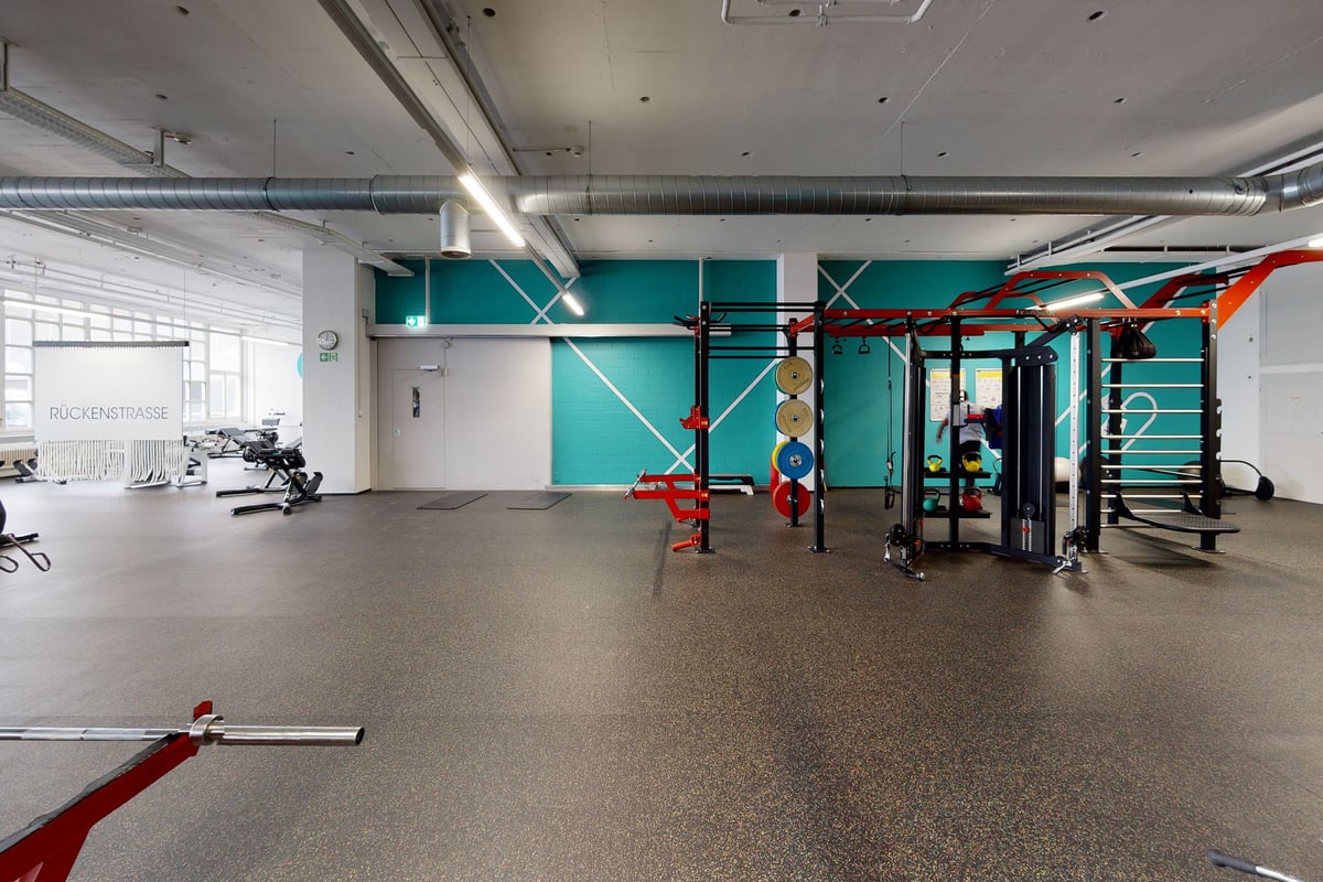 PureGym Bern Bümpliz: Studio de gym avec appareils de résistance, haltères, supports et murs d'accent bleu sarcelle brillant.