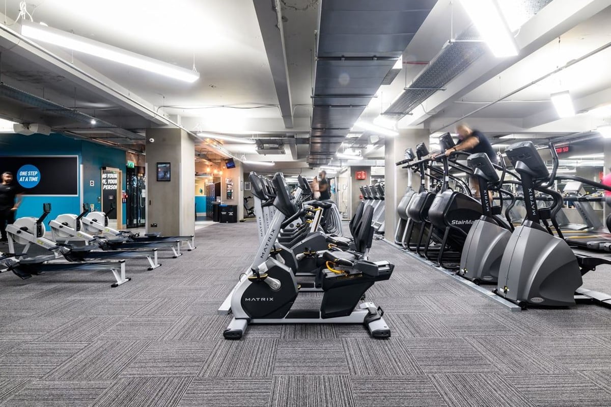 PureGym London Lewisham: Rows of elliptical machines, arc trainers, benches, and freeweights in a dimly lit fitness studio.