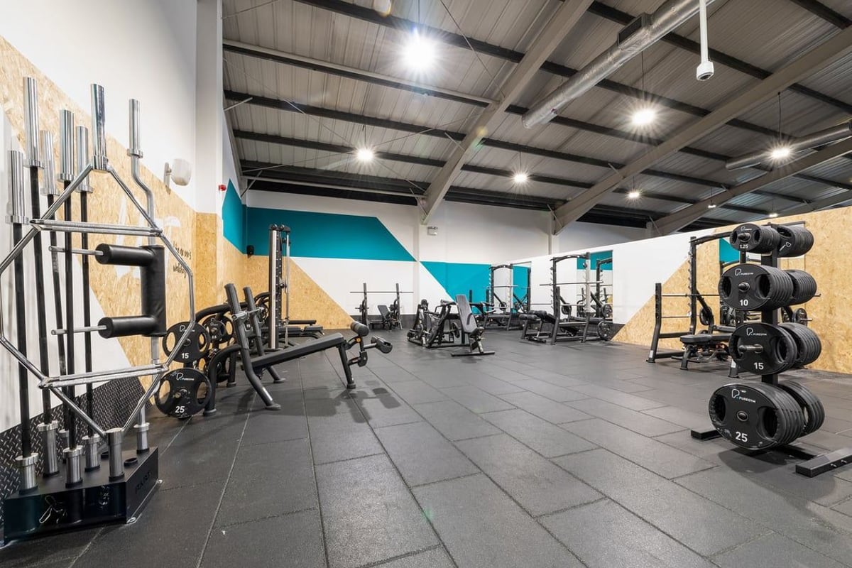 PureGym Leeds Bramley: Fitness studio with weight racks, barbells, squat racks, weight plates, and padded flooring.