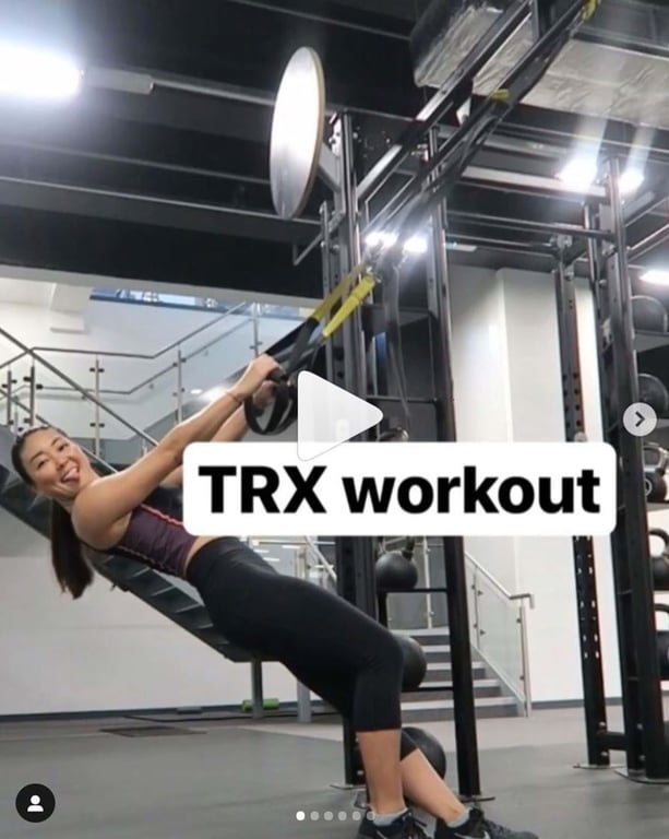 Woman doing TRX workout in gym with stairs and exercise equipment in background