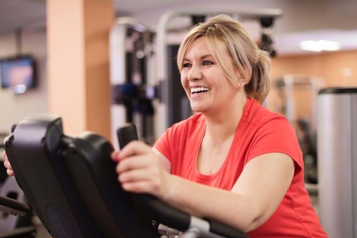 Woman in red shirt smiling while using exercise machine in gym