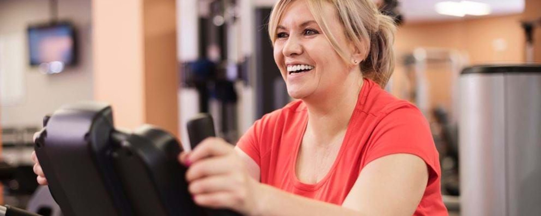 Woman in red shirt smiling while using exercise machine in gym