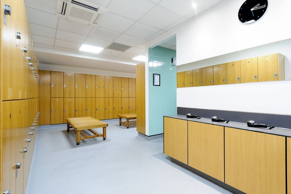 PureGym Billericay: Wooden lockers, benches, and changing cubicles in a gym changing room.