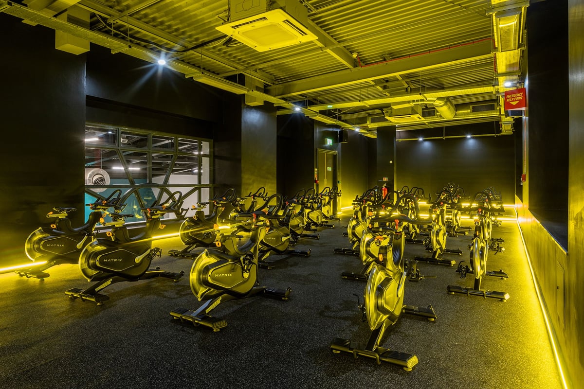 PureGym Southampton Bitterne: Rows of stationary bikes and spin cycles in a dimly lit studio with yellow accent lighting.