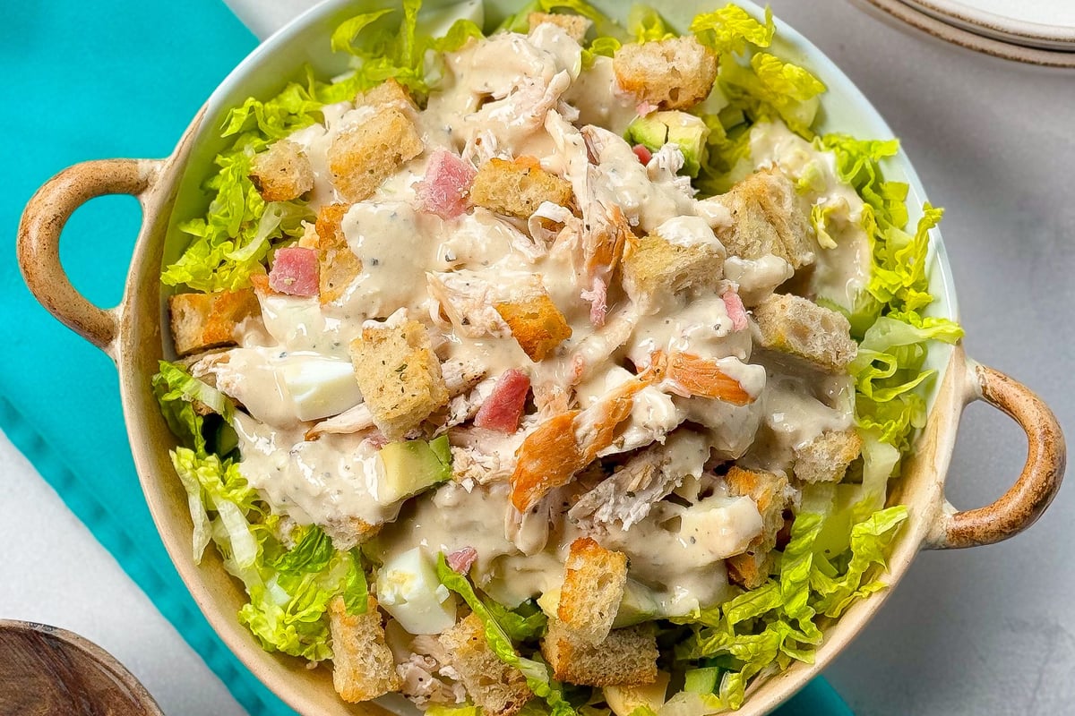 Bowl of Caesar salad with lettuce, croutons, chicken, ham, and creamy dressing