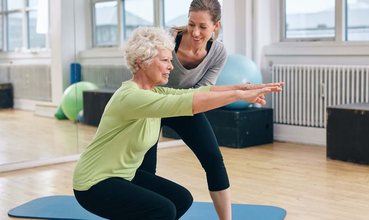 Older woman doing squats with trainer guiding her in gym studio