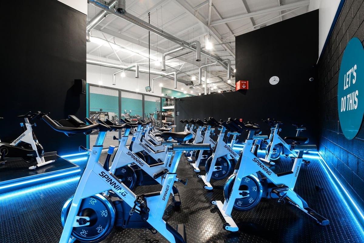 PureGym Exeter Bishops Court: Rows of stationary bikes with neon lighting in a dimly lit studio space.