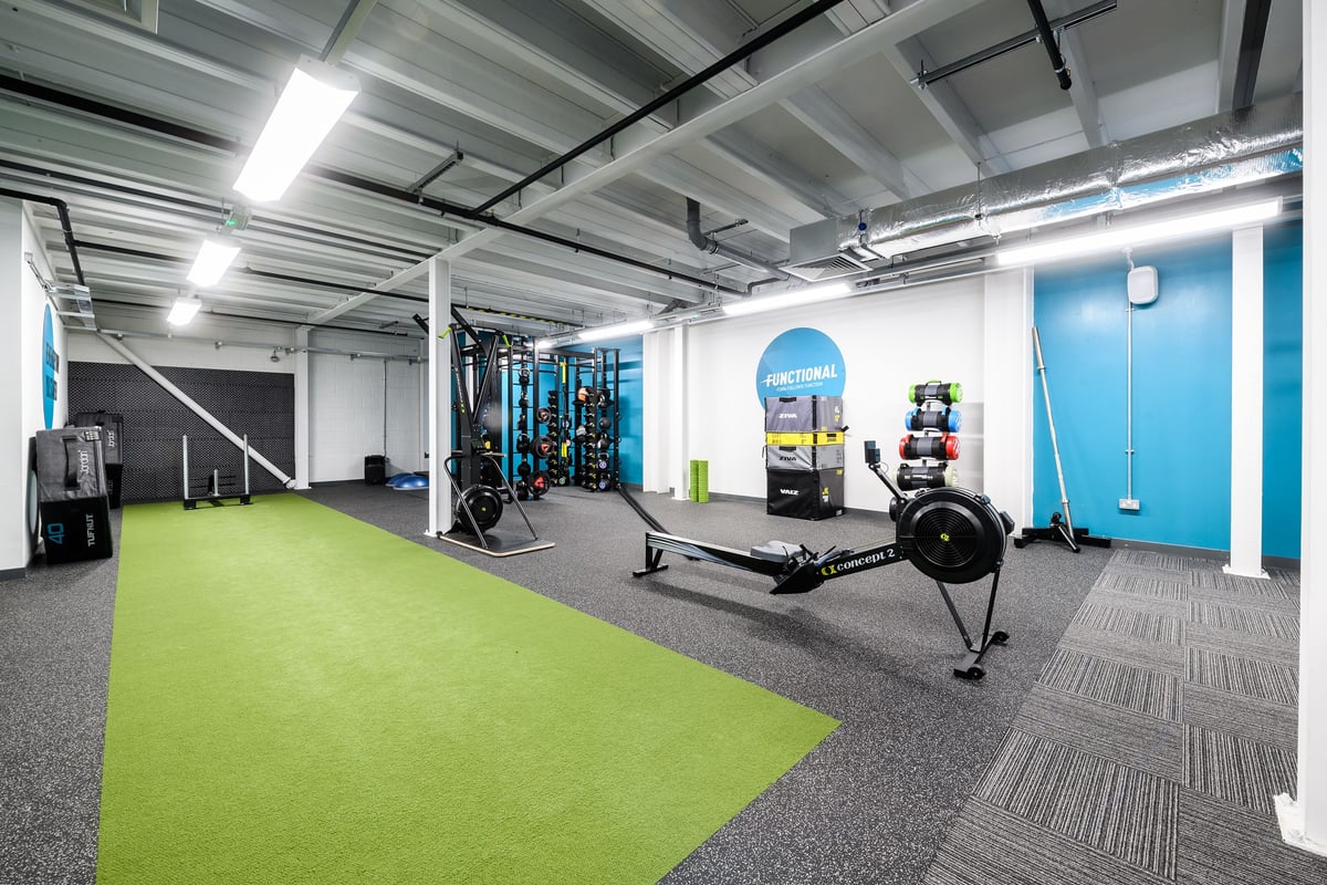 PureGym Glasgow Silverburn: Weight racks, kettlebells, rowing machine, turf area, with exposed ceiling ducts and pipes.