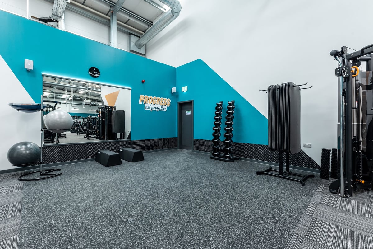 PureGym Dumfries: Teal room with weights, stability balls, racks, rubberized flooring for functional training.