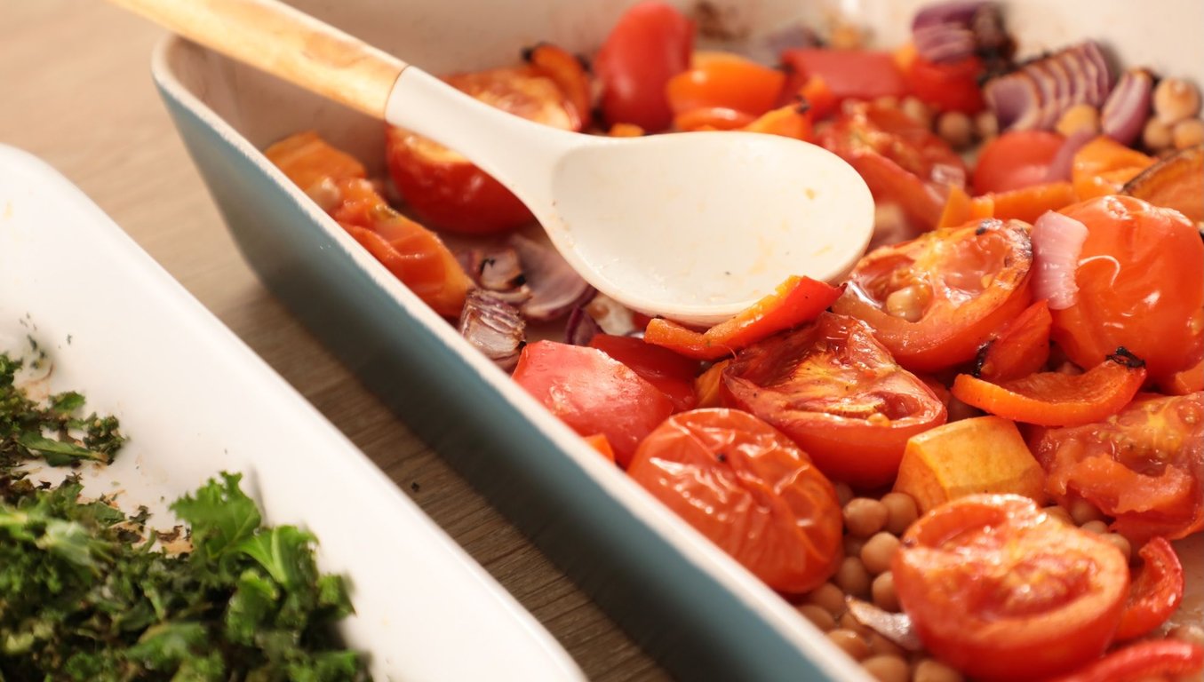Roasted red peppers, tomatoes, chickpeas and sliced red onion in baking tray with spoon